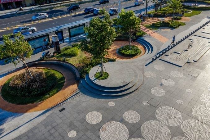 Stedelijk plein met bomen, zittrappen, bushalte en drukke weg